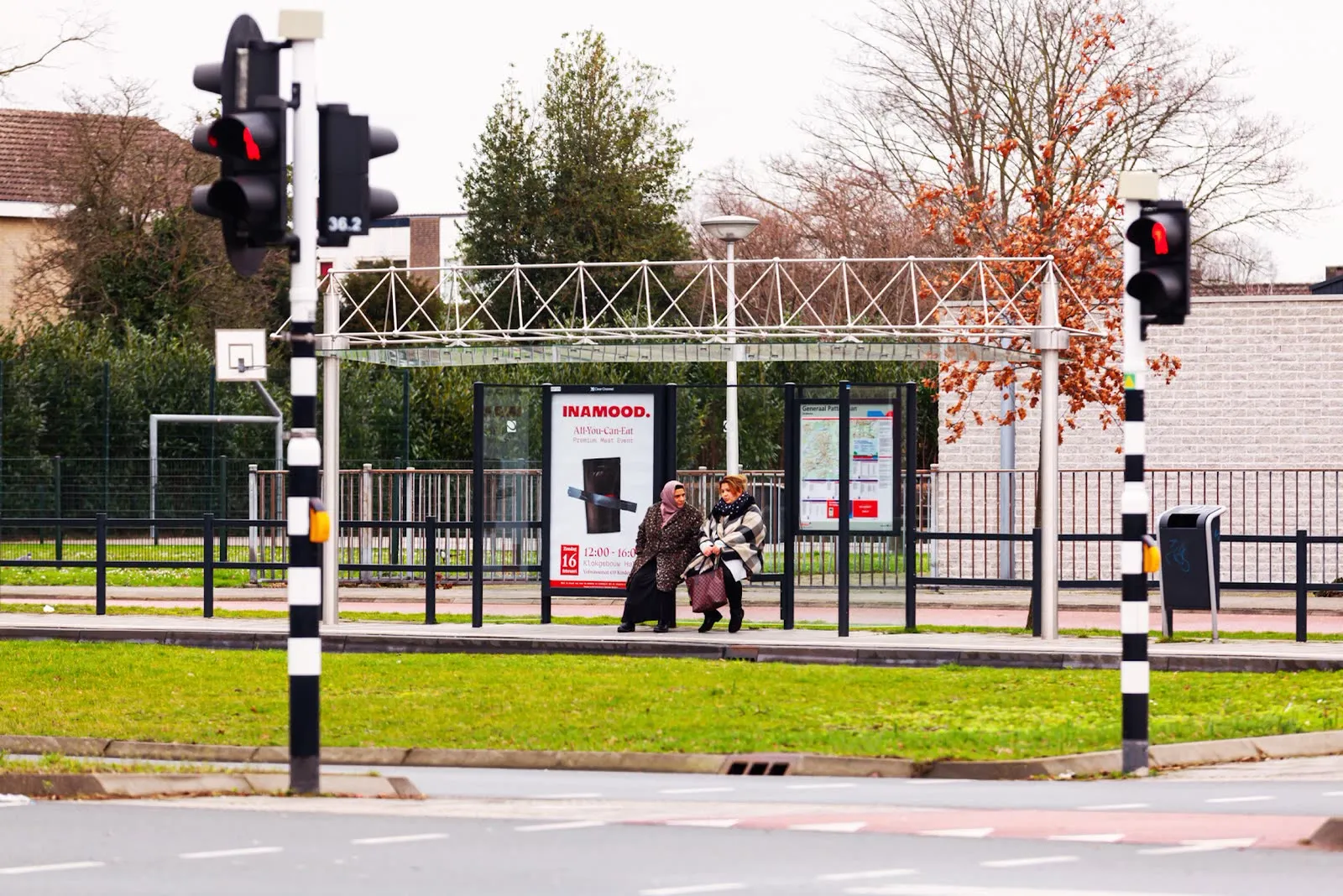 Two people passing an INAMOOD abri poster at a crossing