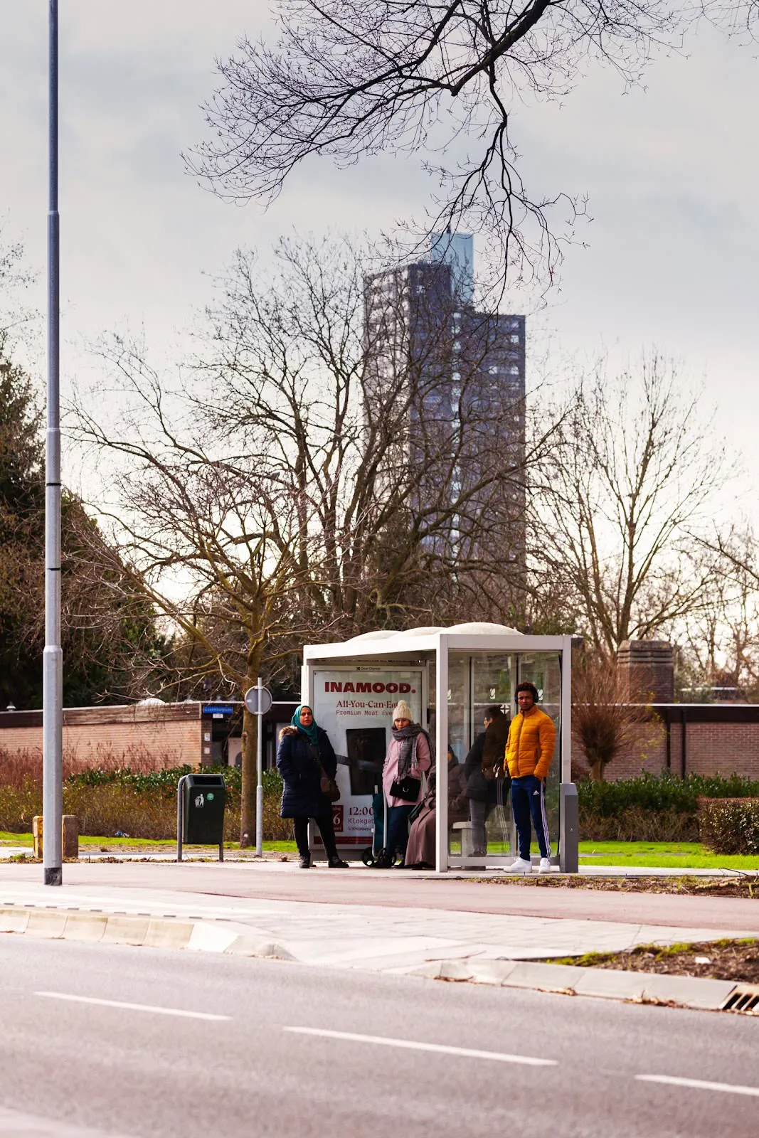 People waiting at a bus stop carrying the INAMOOD event poster
