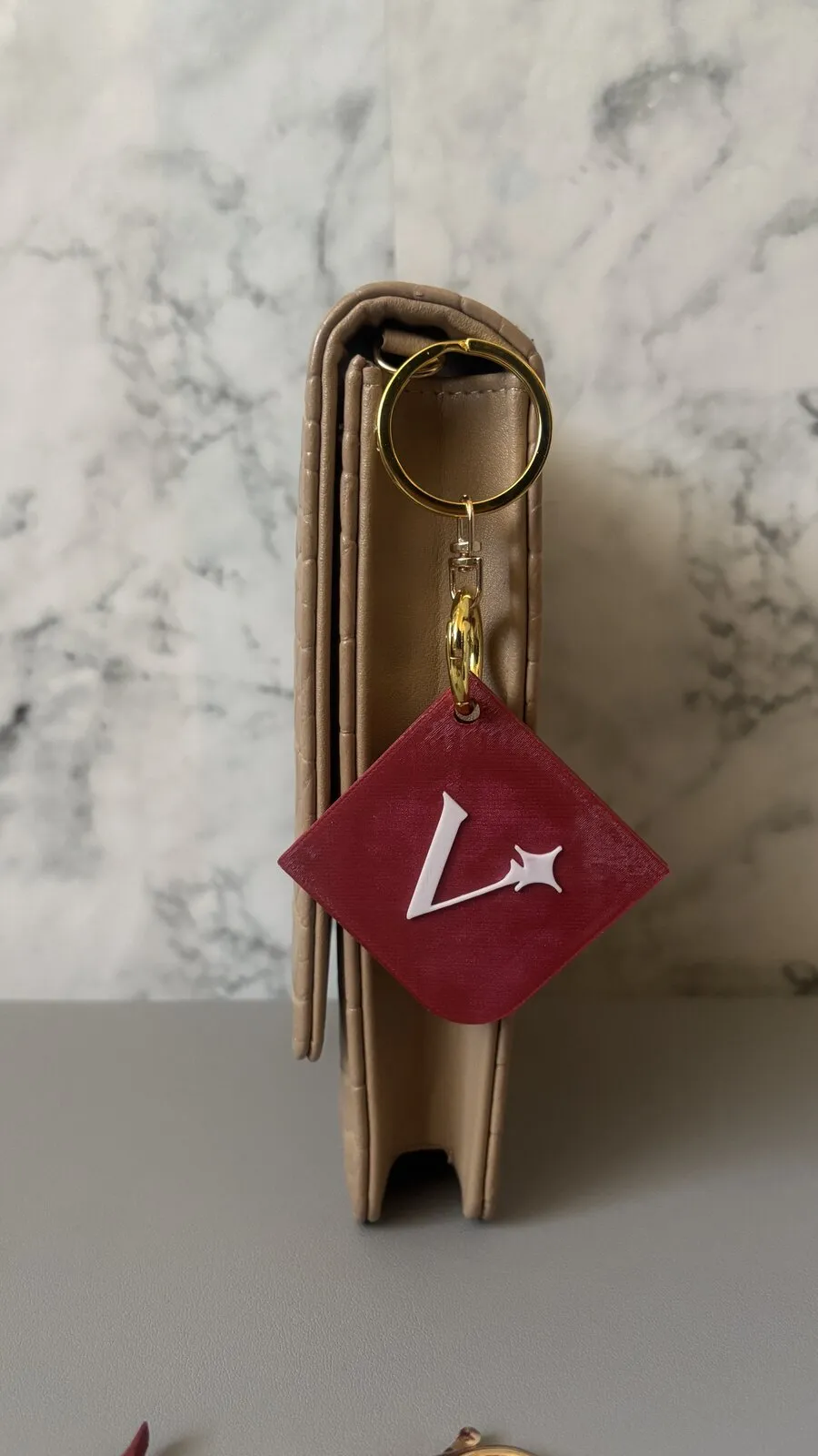 De Beleevd-sleutelhanger: een bordeauxrode ruit met een witte ster, aan een beige tas