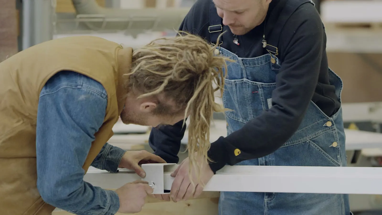 Twee makers gebogen over dezelfde lat hout aan de werkbank