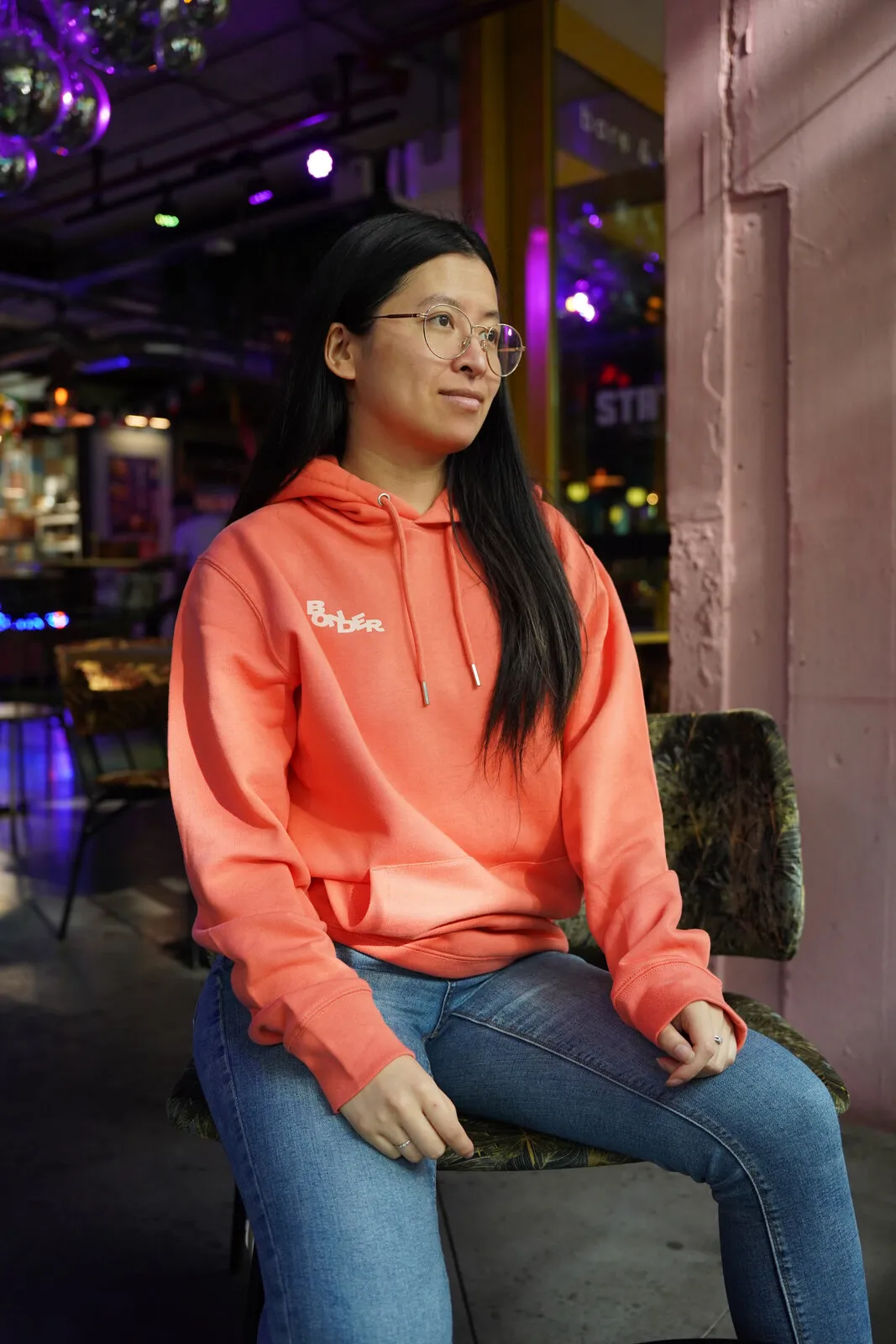 Zittend in de koraalrode hoodie, met het kleine logo op de borst