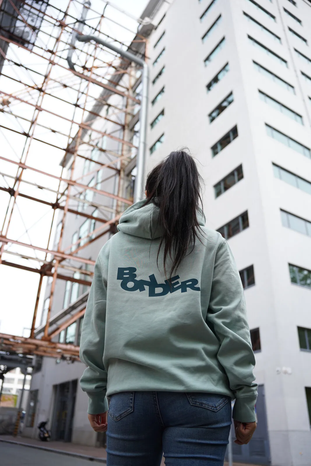 De saliegroene Bonder-hoodie van achteren, met het logo in petrol