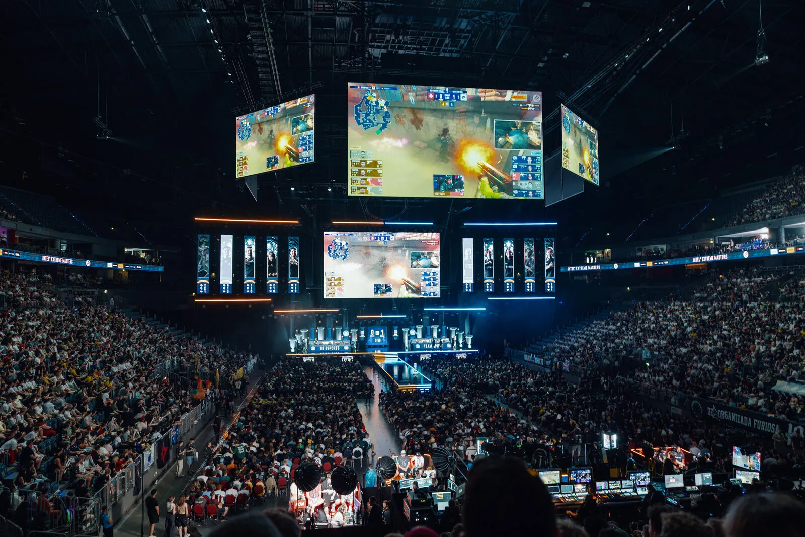 The arena from the stands: two full tiers, the stage lit blue, the game running on the screens overhead