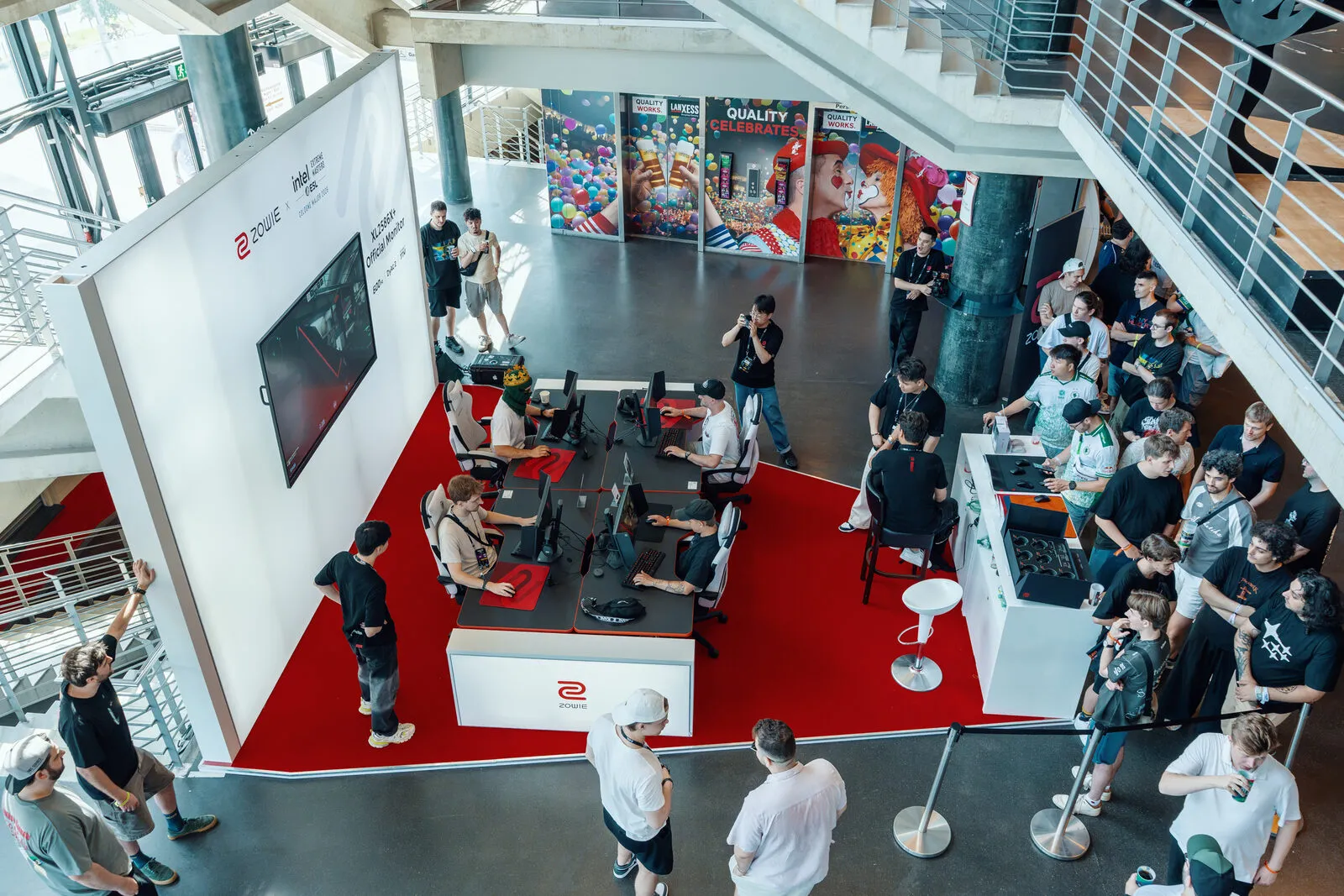 The ZOWIE stand from the balcony above: red floor, a row of playing stations, and a crowd around three sides