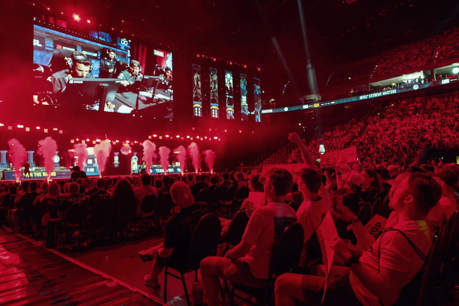 The crowd washed in red light during a round, arms up along the whole tier