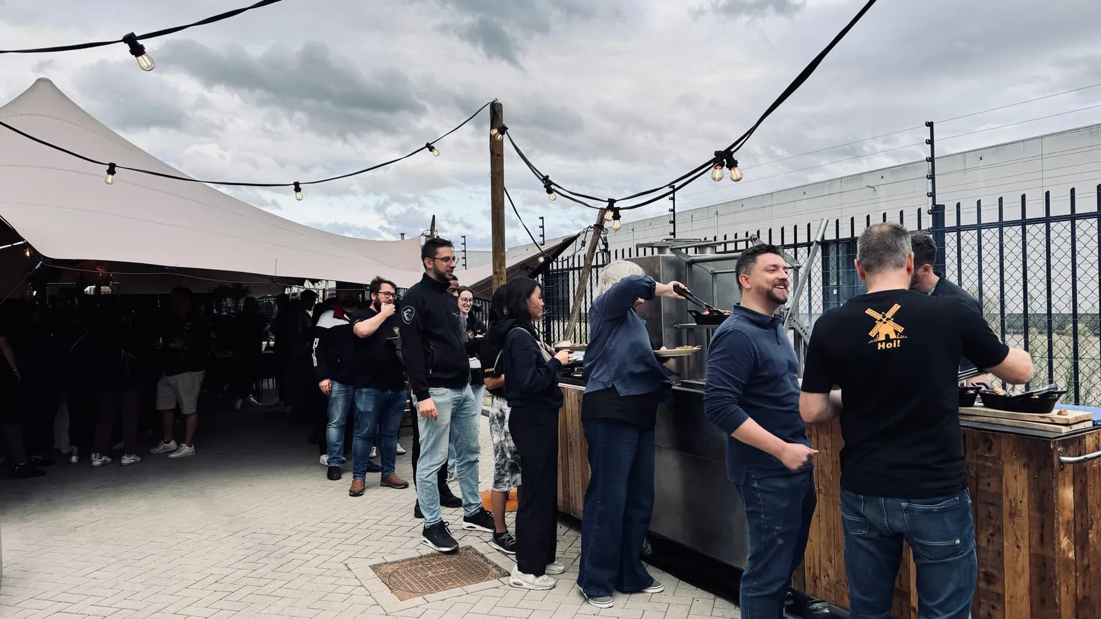 De borrel buiten onder lichtsnoeren, het team in shirts aan de bar