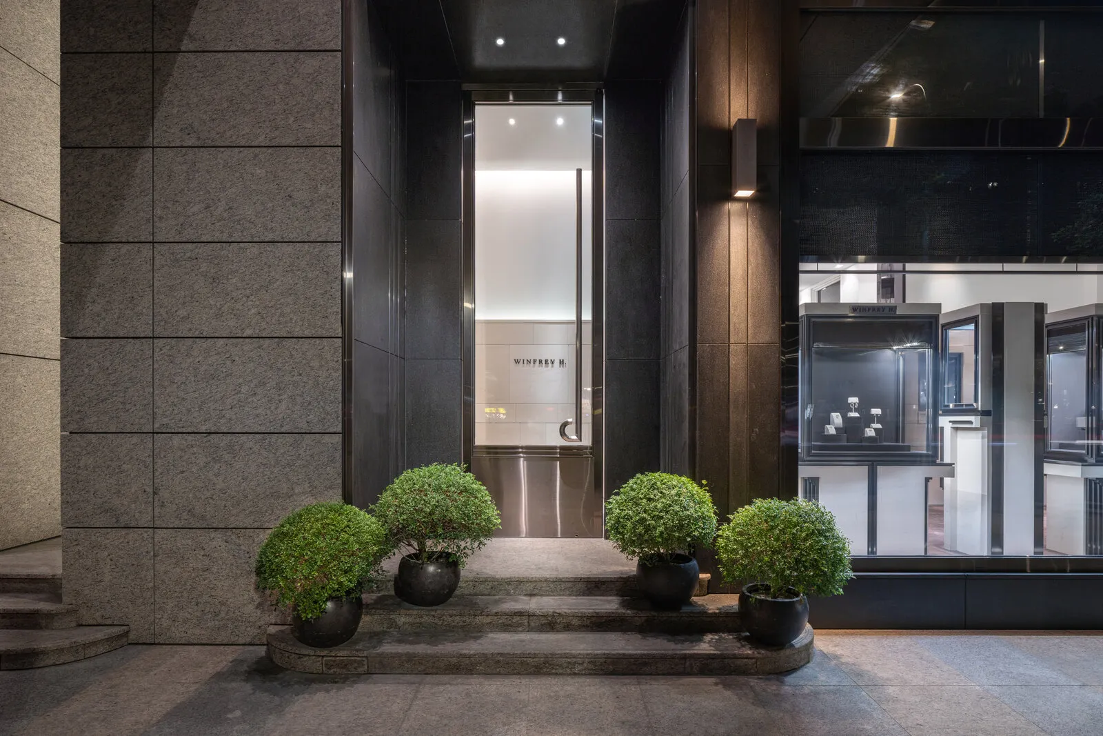 The store entrance at street level, the new sign lit at the end of the passage