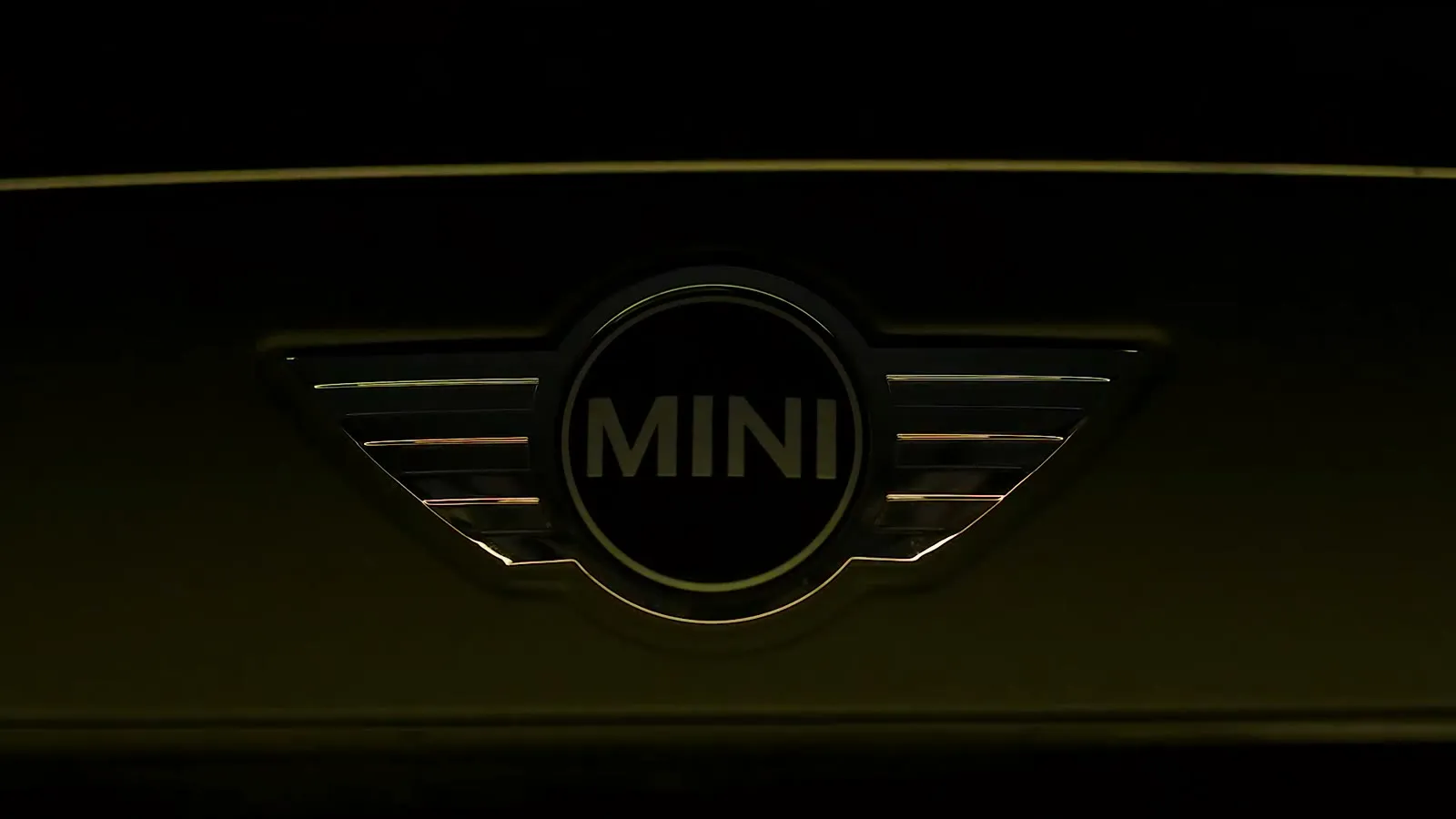 The MINI badge picked out in low gold light on a black bonnet