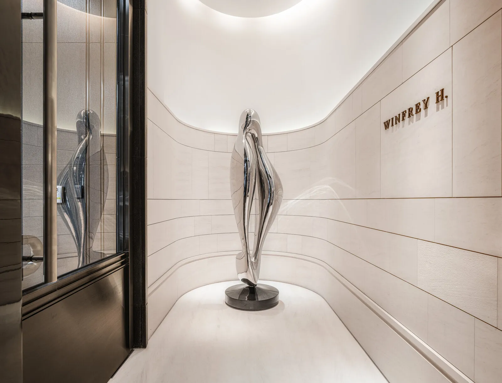 The wordmark on the curved stone wall of the entrance hall, beside a polished steel sculpture