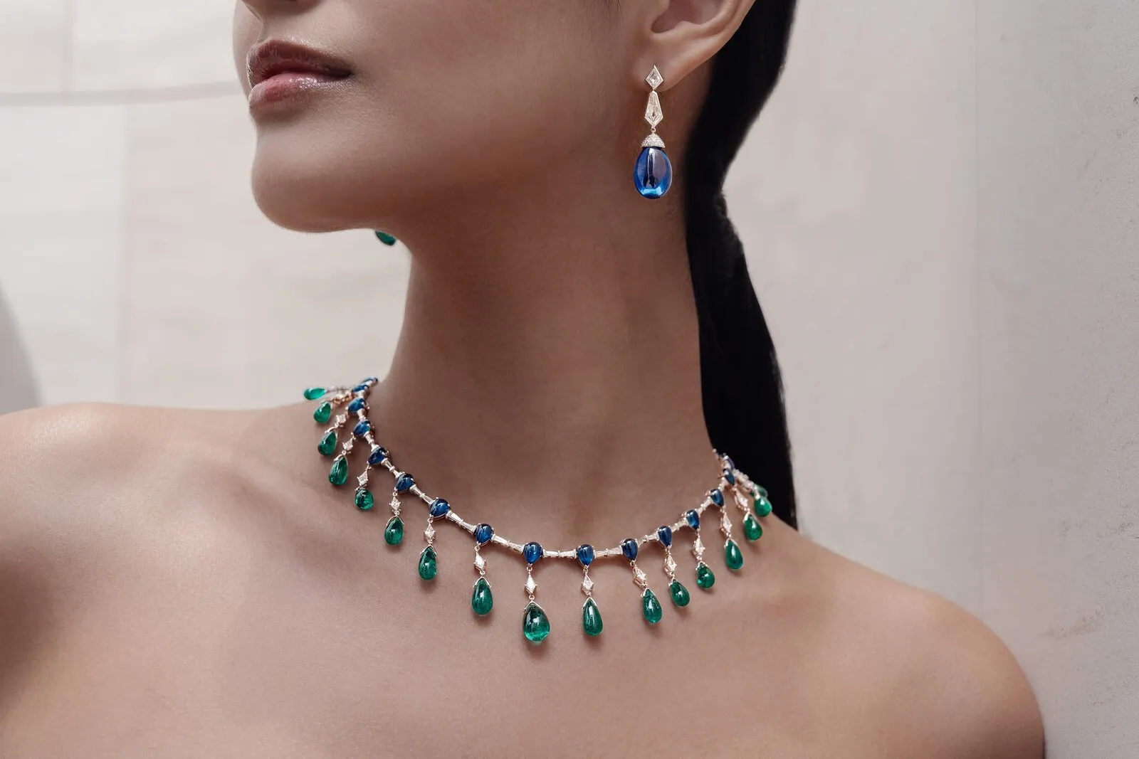 Emerald and sapphire cabochon necklace with matching drop earring, worn on the neck against pale stone