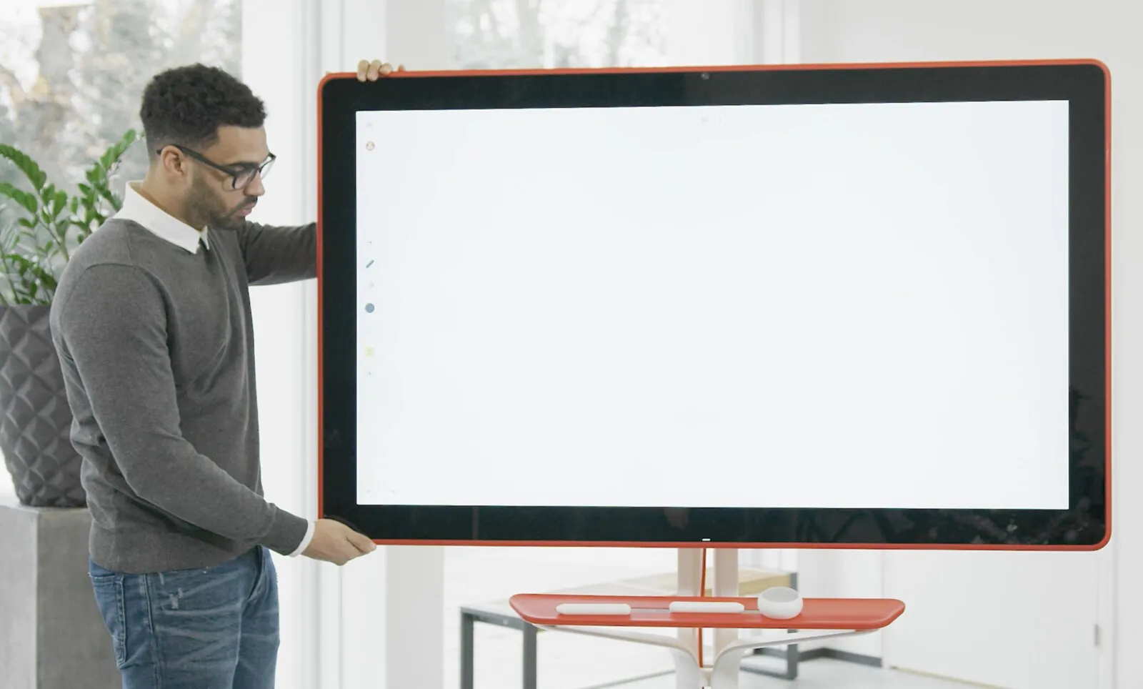 A man setting up a Google Jamboard in a bright office, the screen still empty
