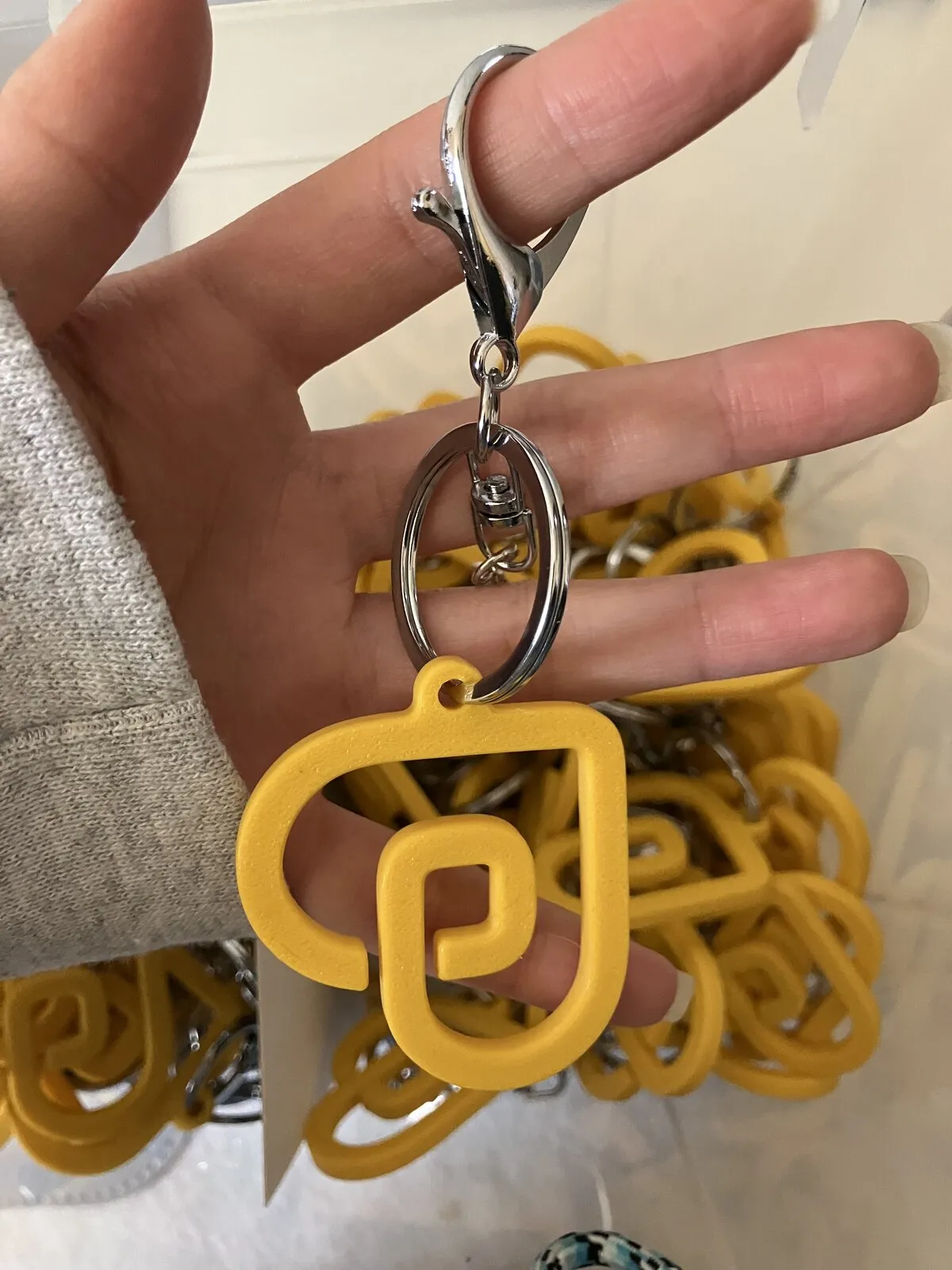 Een hand houdt een gele 3D-geprinte Draaijer Heyday-sleutelhanger aan een zilveren karabijnhaak