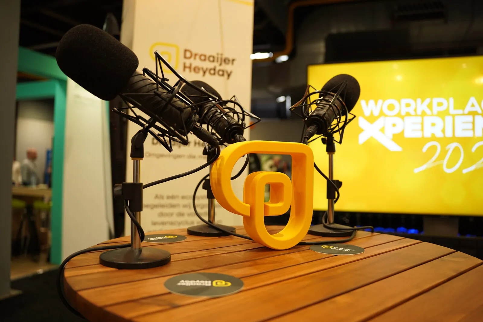Het 3D-geprinte gele beeldmerk tussen vier microfoons op de houten podcasttafel