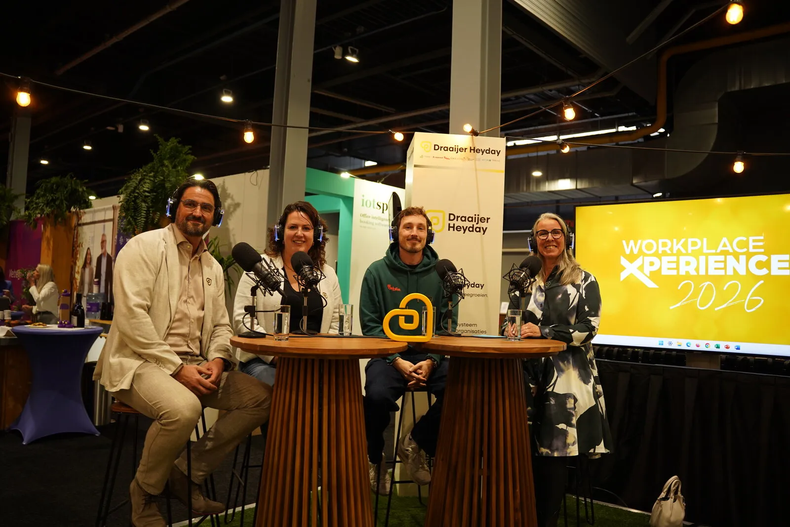 Vier gasten aan de podcasttafel, met het beeldmerk tussen hen in