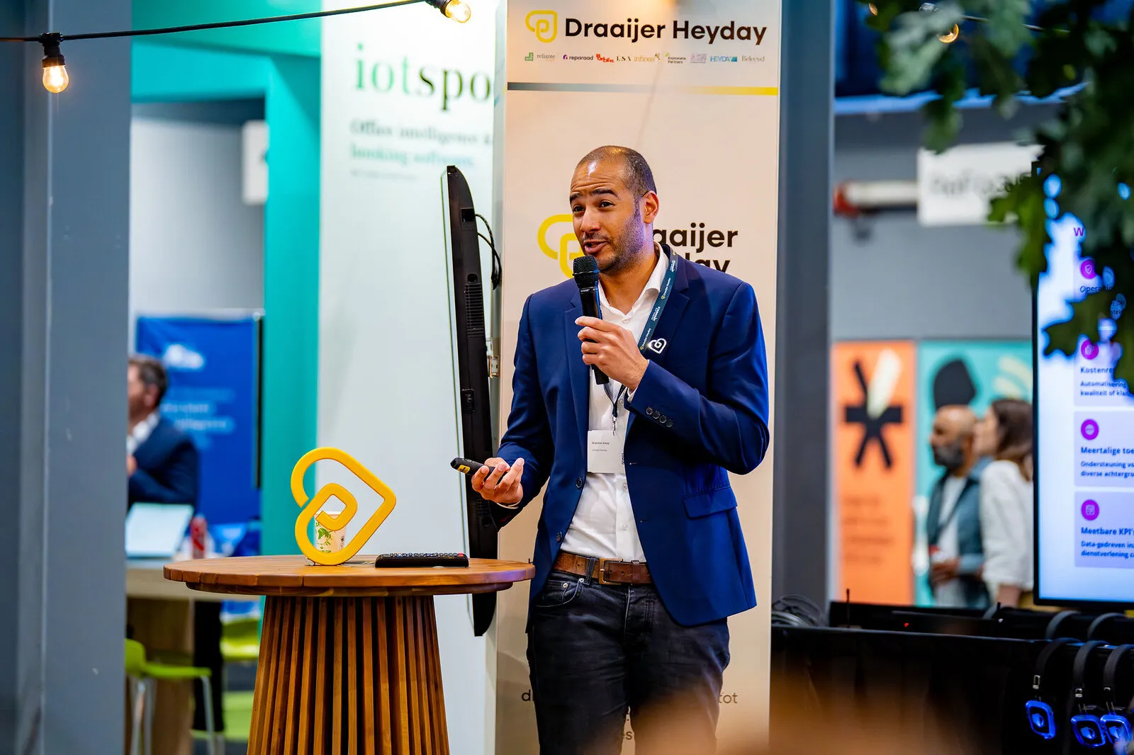 Een spreker met microfoon naast de podcasttafel met het beeldmerk