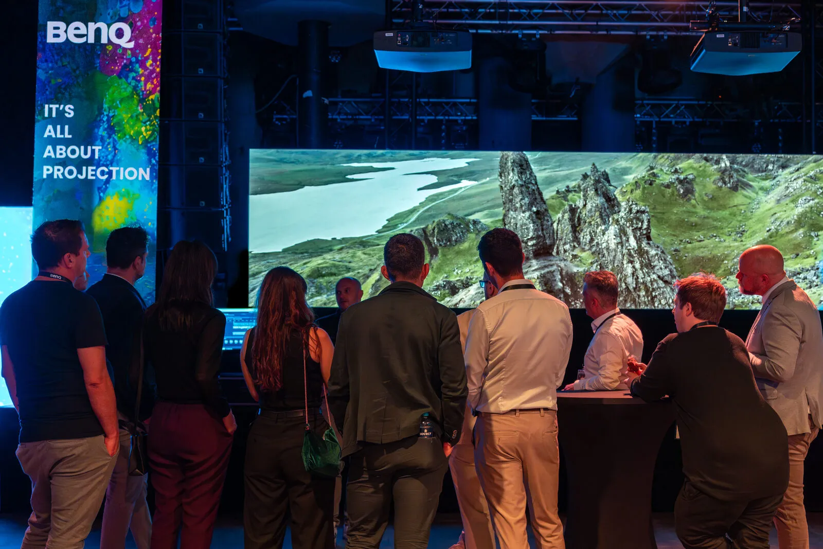 Guests in front of a wide blended landscape projection, under the It's All About Projection banner