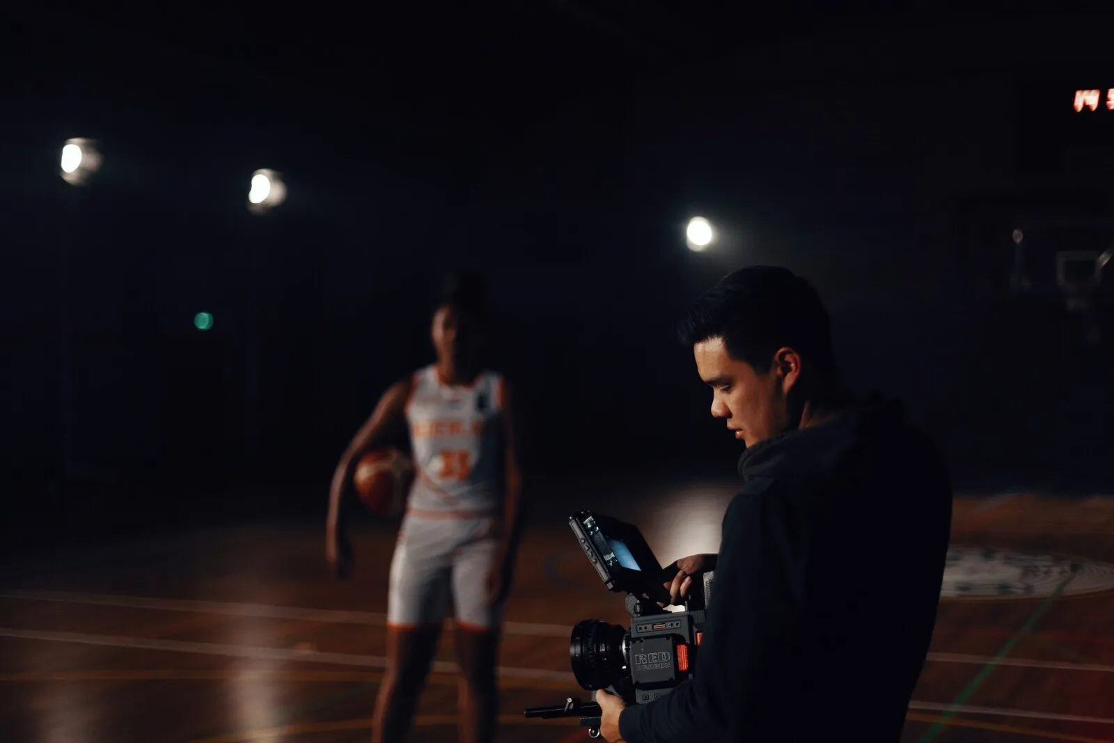 Een cameraman filmt een speler een op een in de donkere zaal