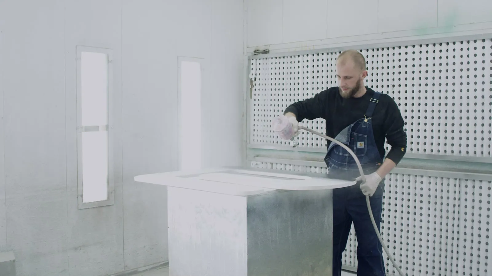Een spuiter werkt een paneel af in de witte spuitcabine