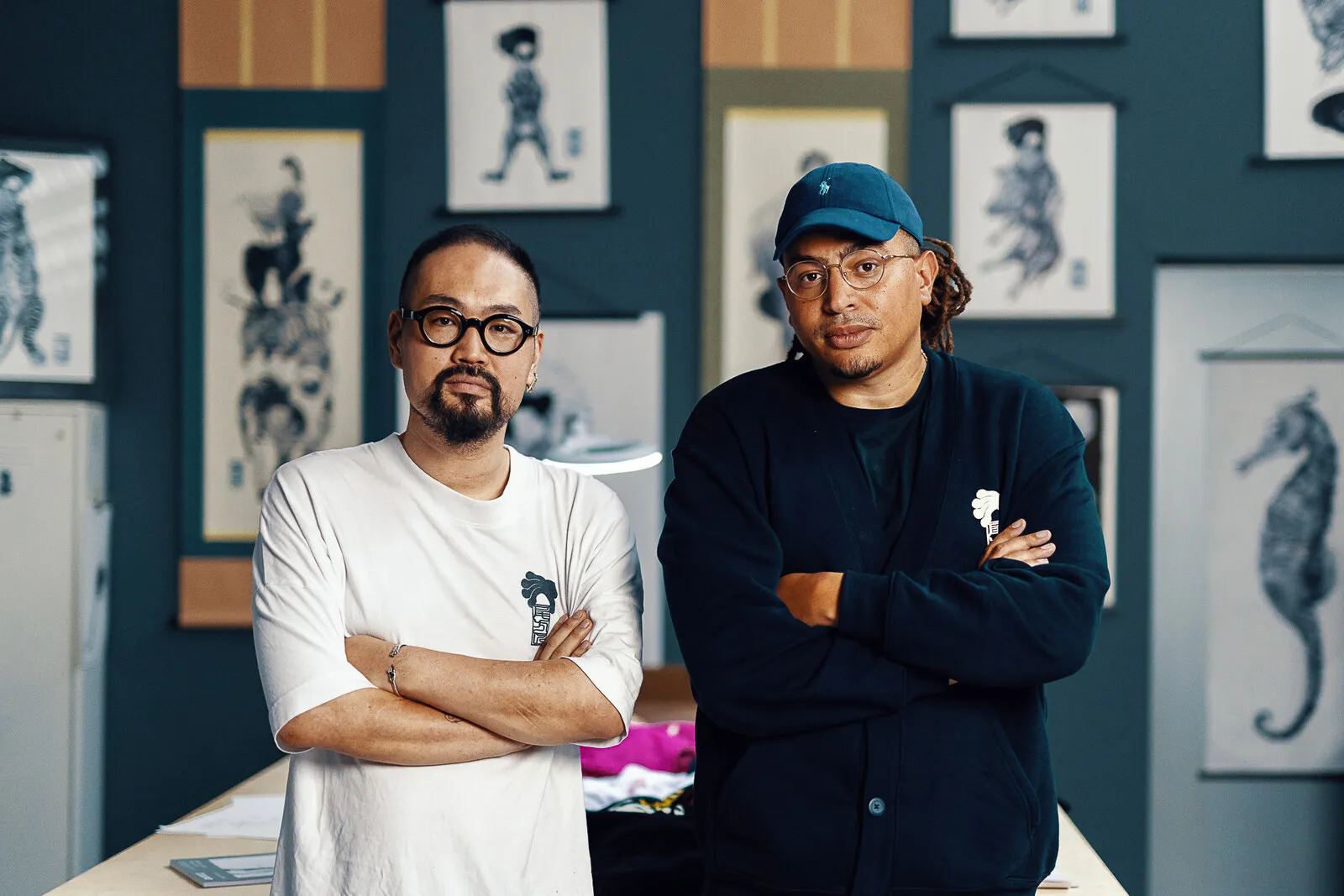 Takumi Ogata and Fresku together in the studio, prints on the wall behind them