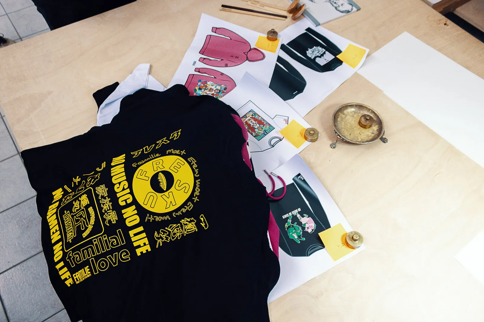 Sample garments laid out beside the printed artwork sheets and tech drawings