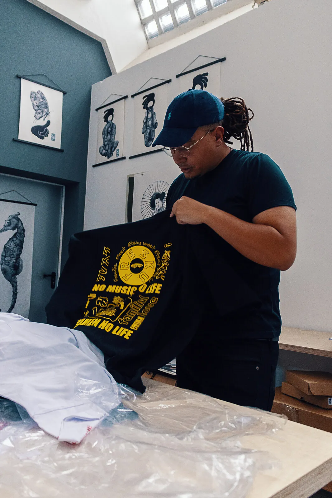 Fresku holding up the black tee, the yellow no music no life print across it