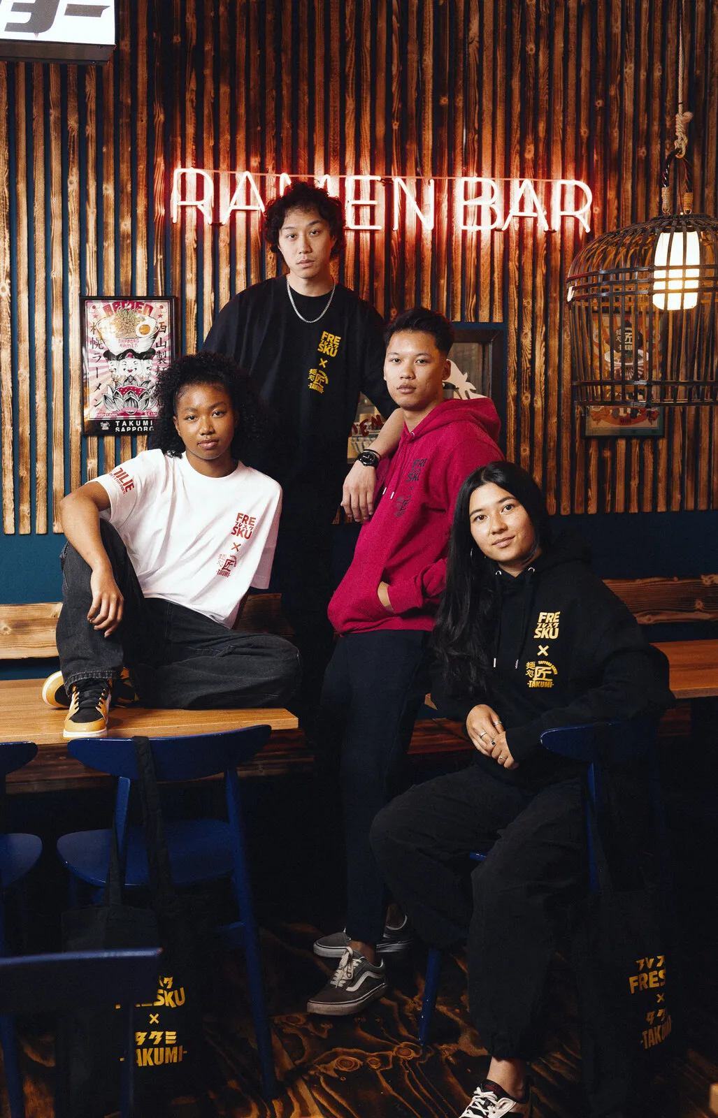 Four guests wearing the collection under the ramen bar neon inside Takumi