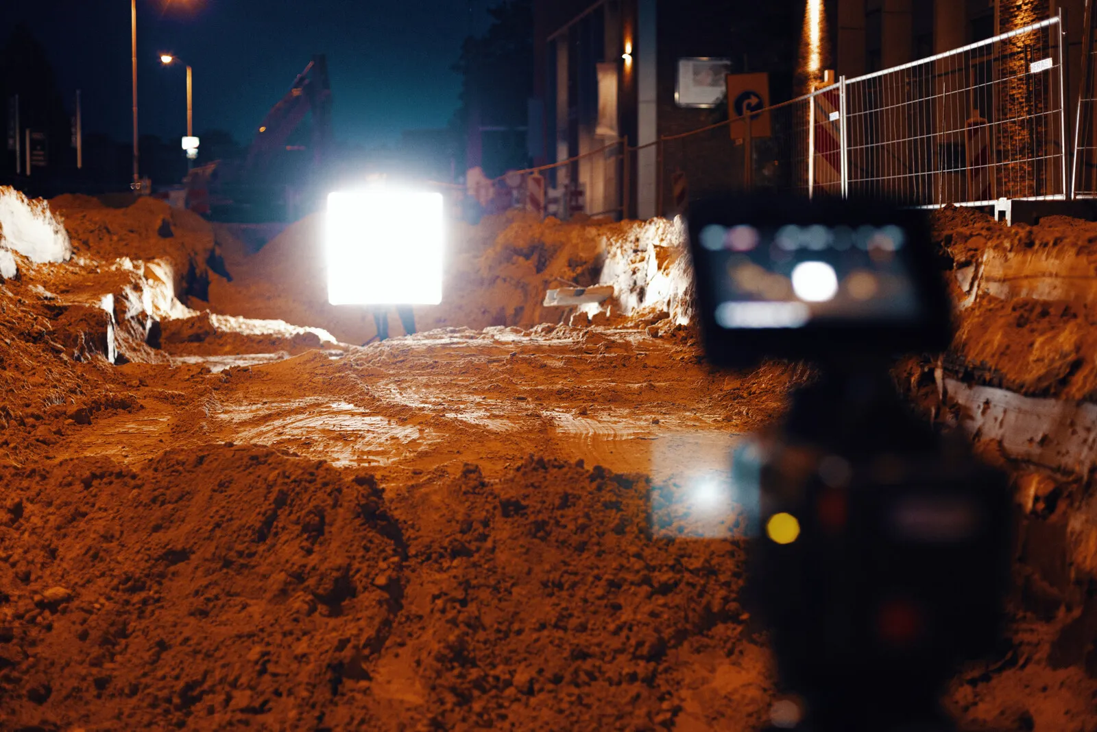 Eén verlicht paneel in een opengebroken straat bij nacht, zand en machines eromheen