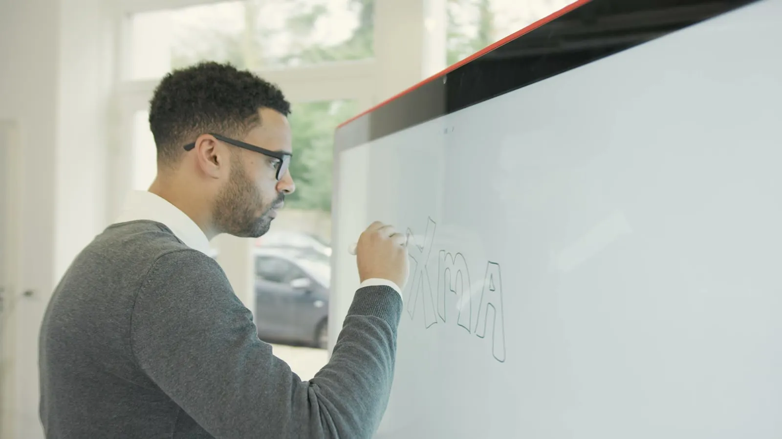 A man drawing on the Jamboard, seen through the glass of the screen